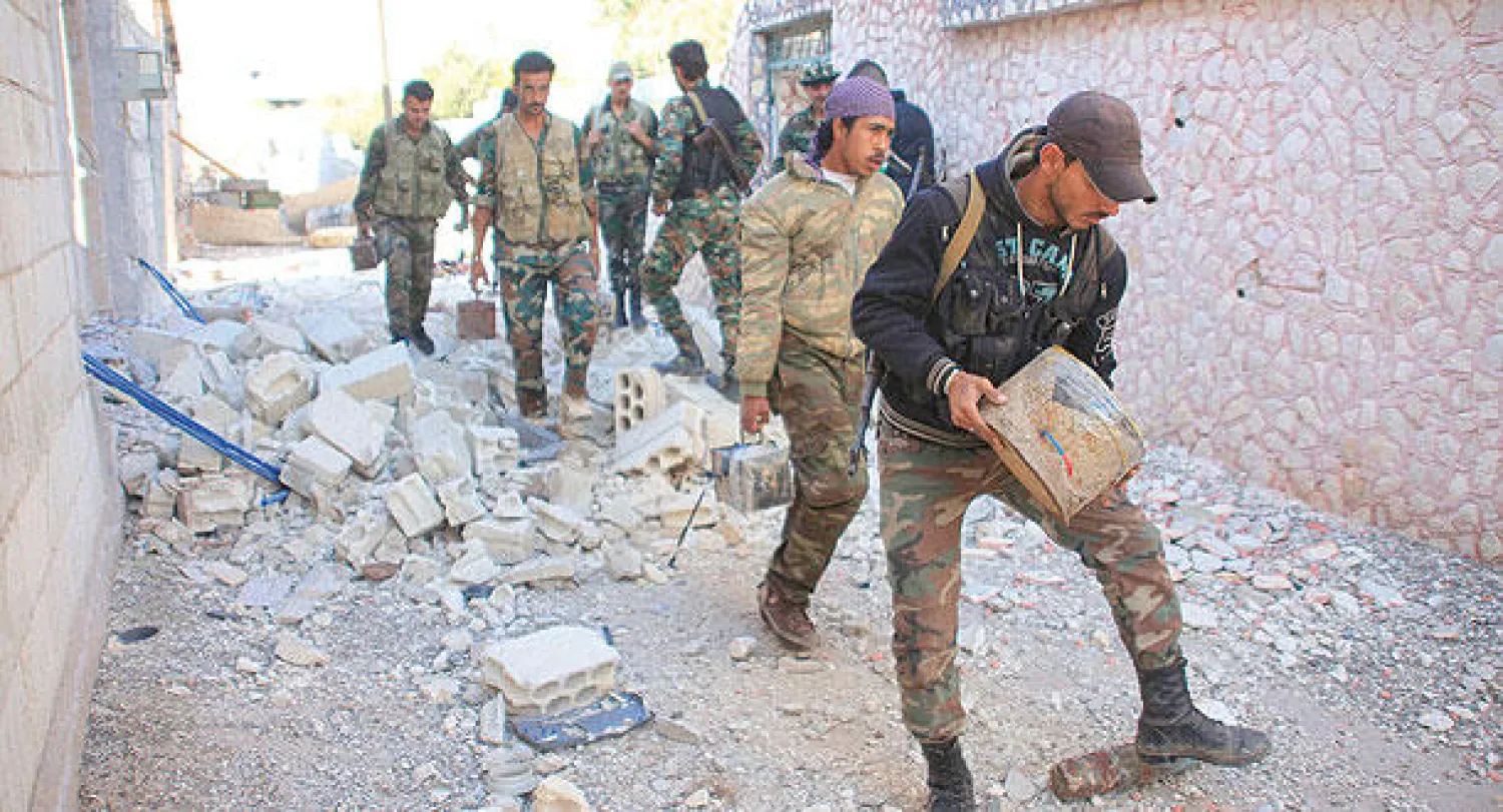 عناصر موالية للنظام السوري تنقل أجساما متفجرة تركها المقاتلون قبل خروجهم من المورك التي استعادها النظام أمس (رويترز)