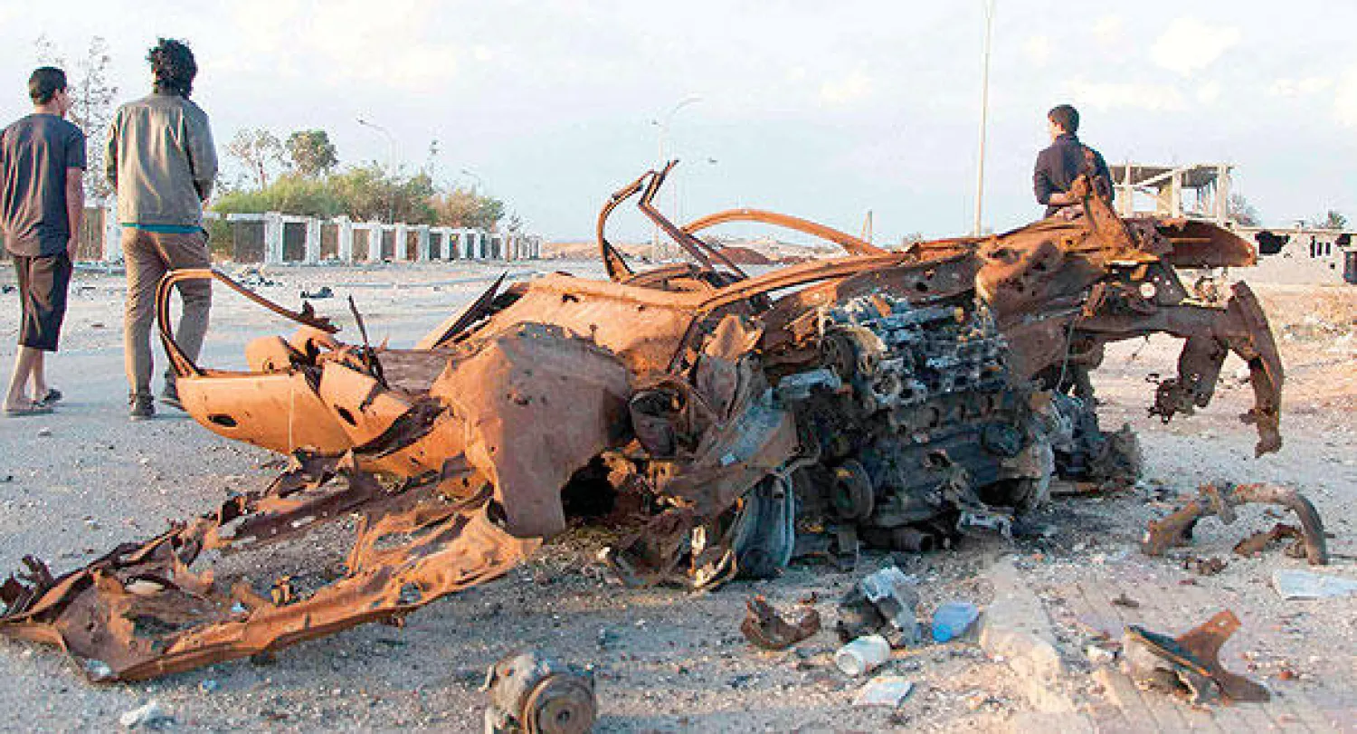 ليبيون بجانب حطام عربية بعد المواجهات التي حدثت في منطقة بنينة في بنغازي أمس (رويترز)