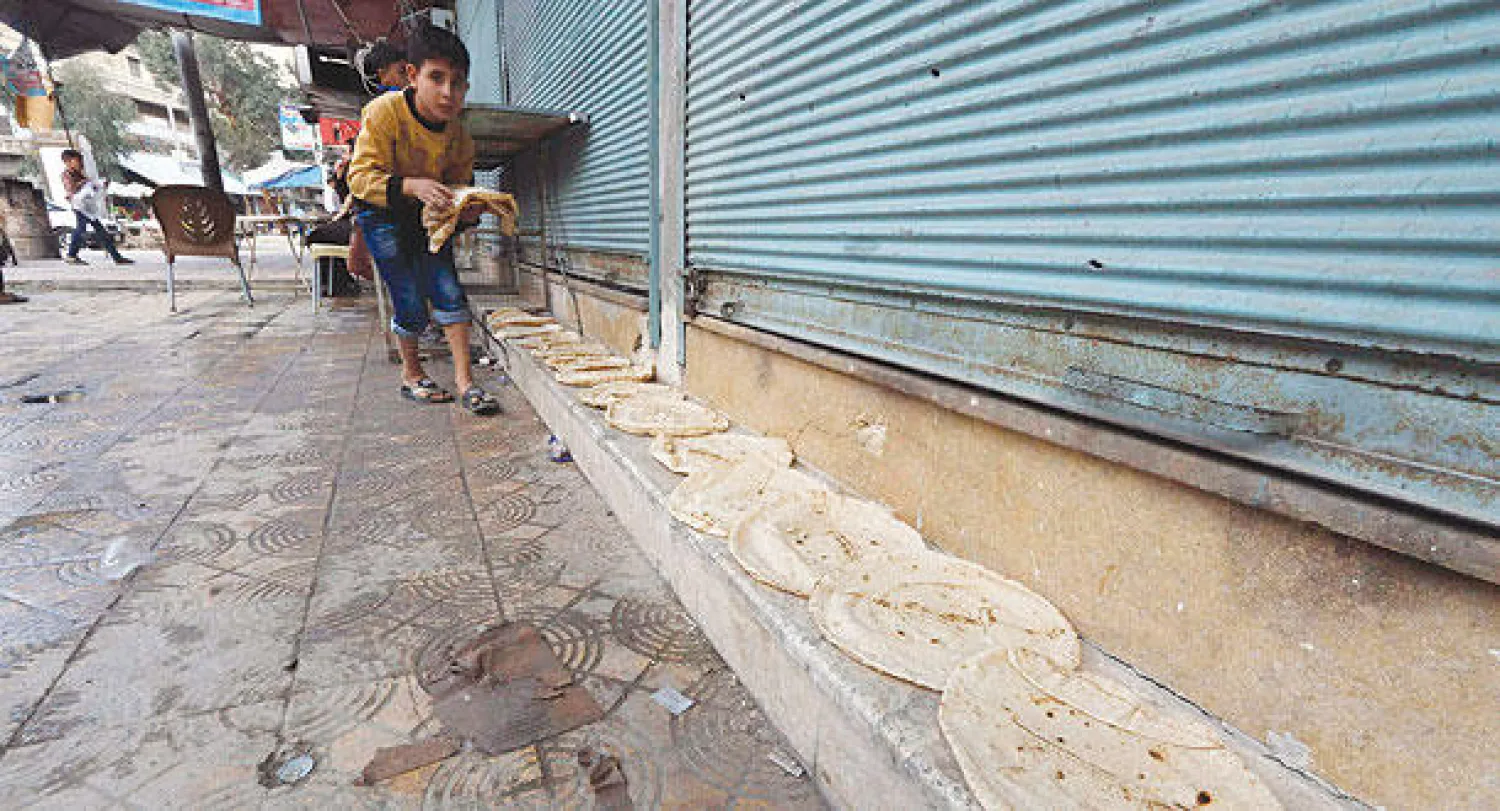 صبي سوري يفرش الخبز الساخن على الأرض كي يبرد قليلا في سوق بحي المشهد بحلب أمس (رويترز)