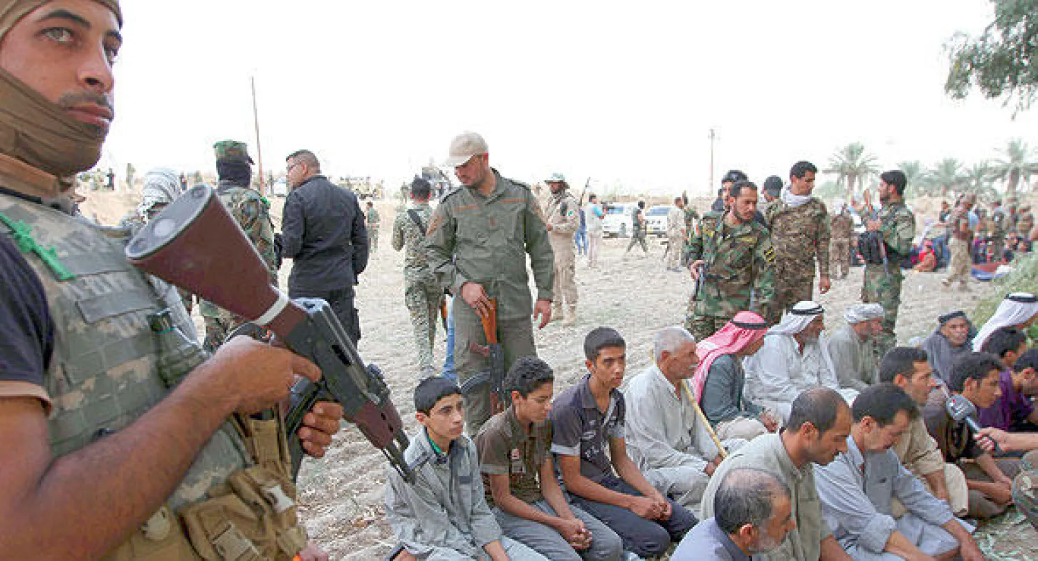 رجال من سكان جرف الصخر يجلسون على الأرض محاطين بمسلحين من «الحشد الشعبي» بعد طرد «داعش» من البلدة الاثنين الماضي (رويترز)