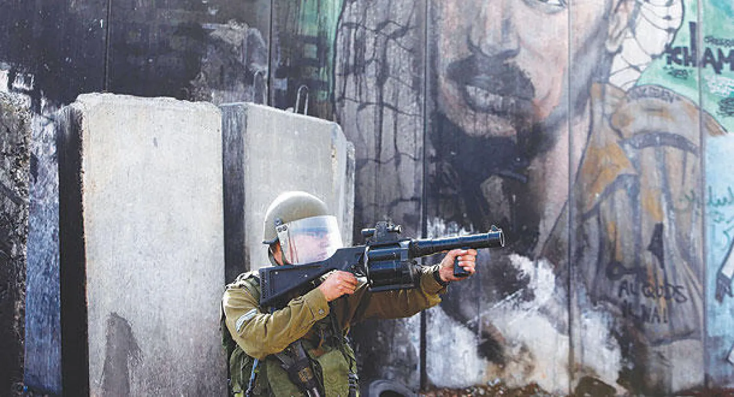 جندي إسرائيلي يوجه سلاحه صوب متظاهرين فلسطيين في رام الله أمس (رويترز)