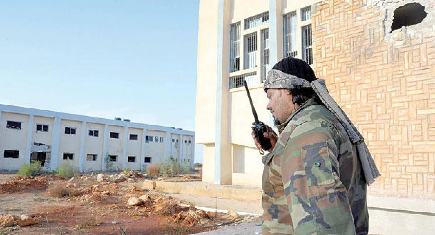 جندي من الجيش الليبي يتحدث في جهاز لاسلكي ويظهر خلفه مبنى ظهرت عليه آثار الاشتباكات مع المسلحين في بنغازي أمس (أ.ب)