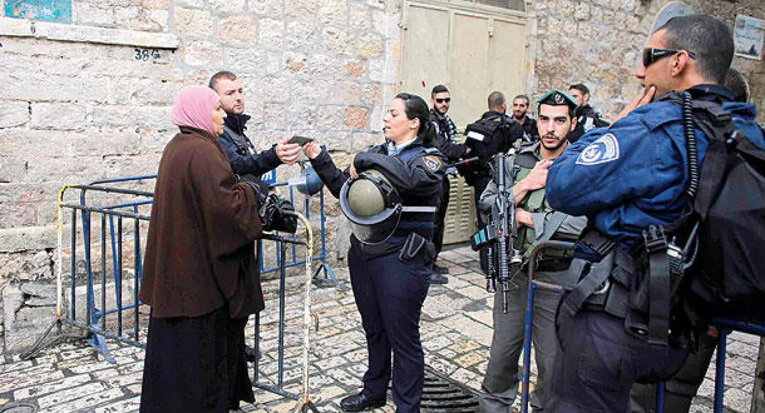 شرطية إسرائيلية تدقق في هوية مواطنة فلسطينية قبل دخولها ساحة المسجد الأقصى (رويترز)
