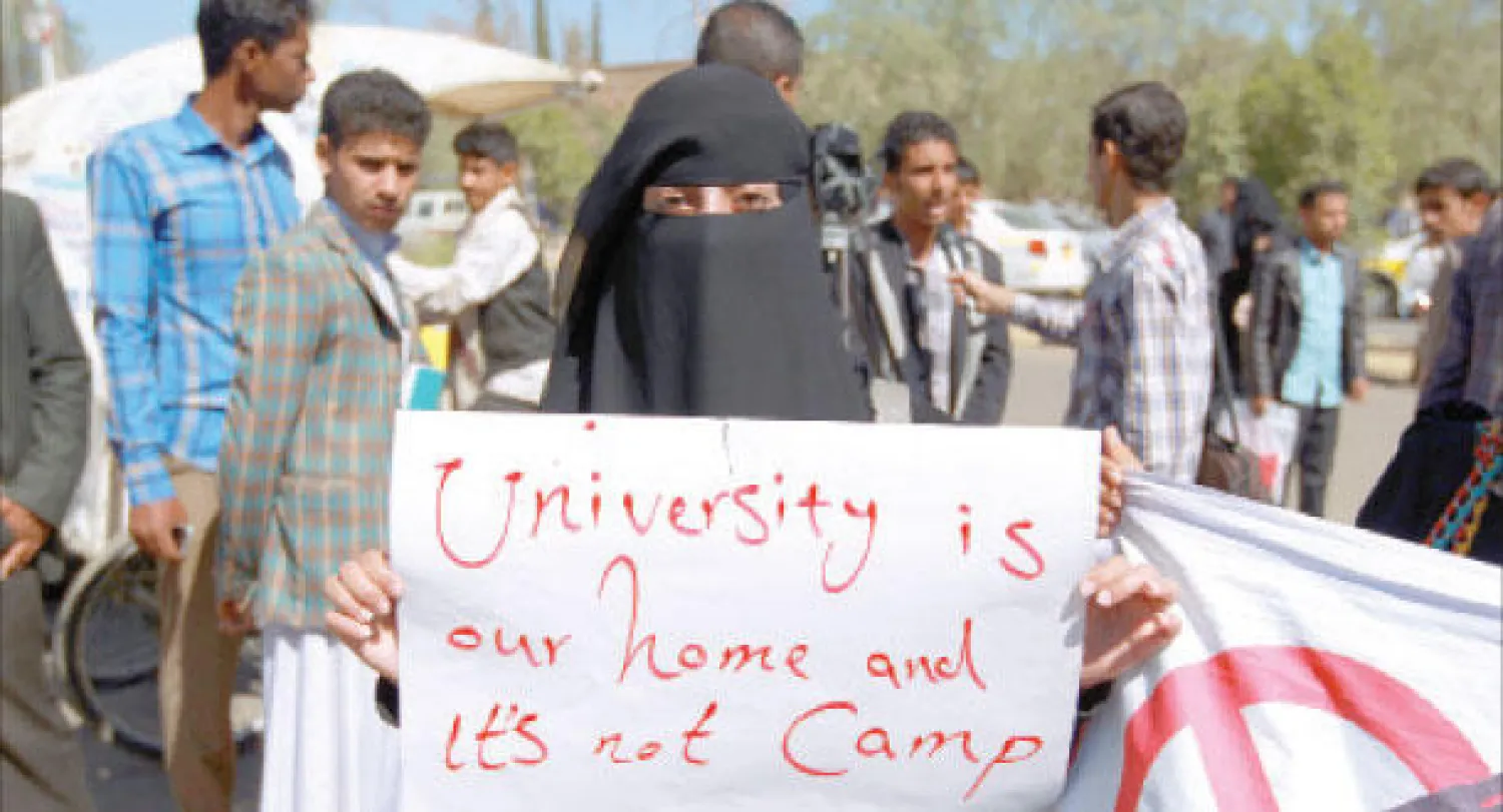 طالبة يمنية تحمل لافتة كتب عليها (الجامعة ليست معسكرا) خلال مسيرة احتجاج ضد الحوثيين بجامعة صنعاء أمس (أ.ف.ب)