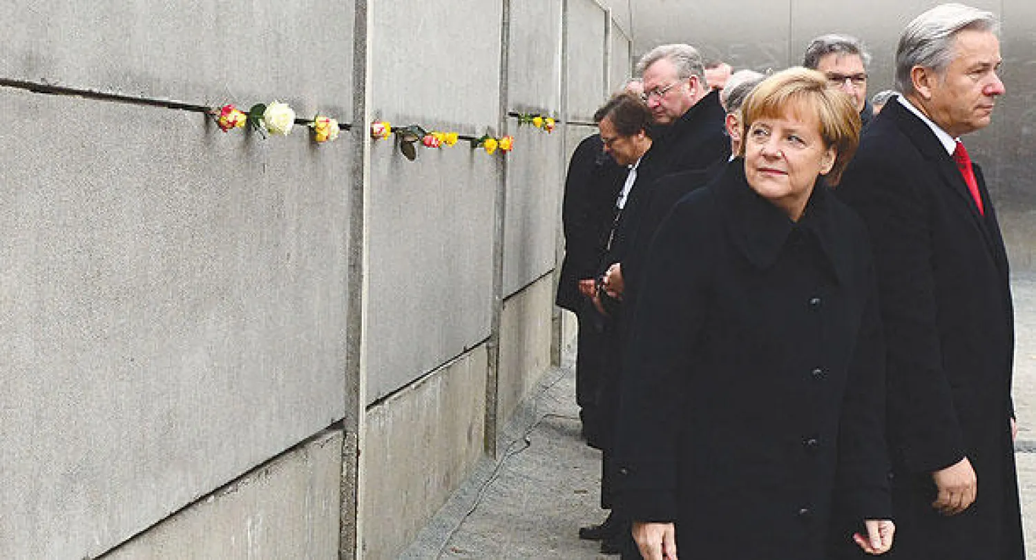 المستشارة الألمانية أنجيلا ميركل تنظر إلى جزء تذكاري من جدار برلين وضعت عليه الزهور ضمن احتفالات أمس (أ.ف.ب)