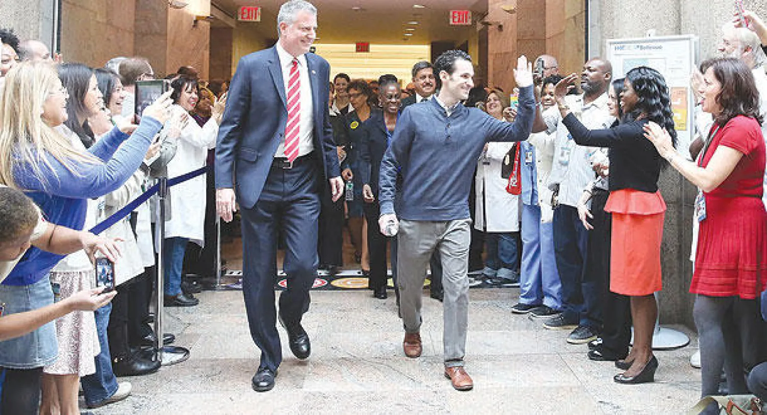 كريغ سبنسر (وسط يمين) الذي أعلن الأطباء شفاءه من «إيبولا» يسير رفقة عمدة نيويورك بيل دي بلاسيو (وسط يسار)  في مستشفى بيليفو بنيويورك أمس (إ.ب.أ)