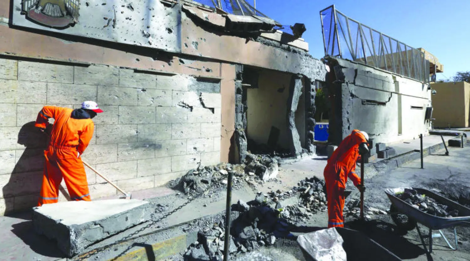 عاملا نظافة خارج مبنى سفارة دولة الإمارات العربية المتحدة  الذي تضرر إثر انفجار سيارة ملغومة  قرب السفارة (أ.ف.ب)