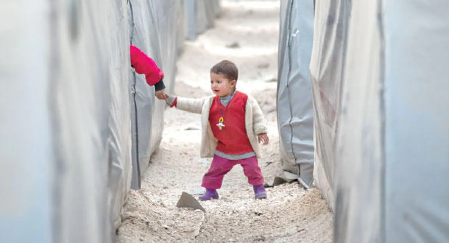 طفل من لاجئي كوباني يمسك بيد طفل آخر يسير بين الخيام في مخيم للاجئين بمنطقة سوروش قرب الحدود التركية - السورية أمس (أ.ب)