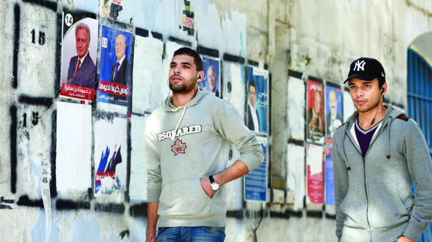 تونسيان يمران بجانب ملصقات انتخابية في العاصمة تونس أمس (أ.ف.ب)