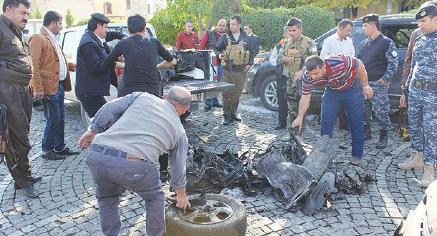 عناصر من أجهزة الأمن الكردية يتفحصون بقايا السيارة التي تم تفجيرها من قبل انتحاري عند بوابة محافظة أربيل («الشرق الأوسط»)