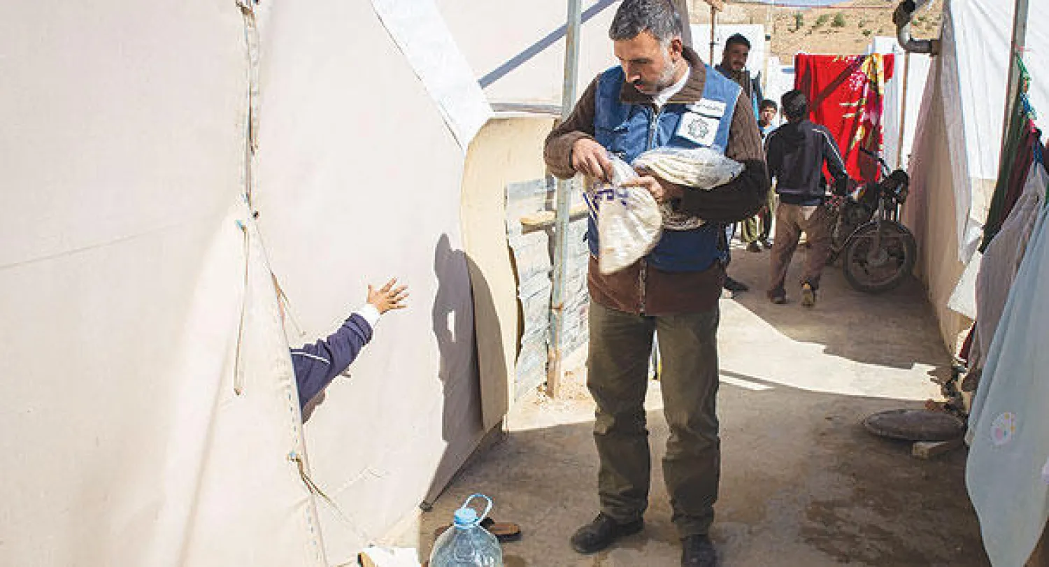 متطوع من منظمة لبنانية غير حكومية يوزع الخبز على سكان مخيم عرسال الشهر الماضي (أ.ف.ب)