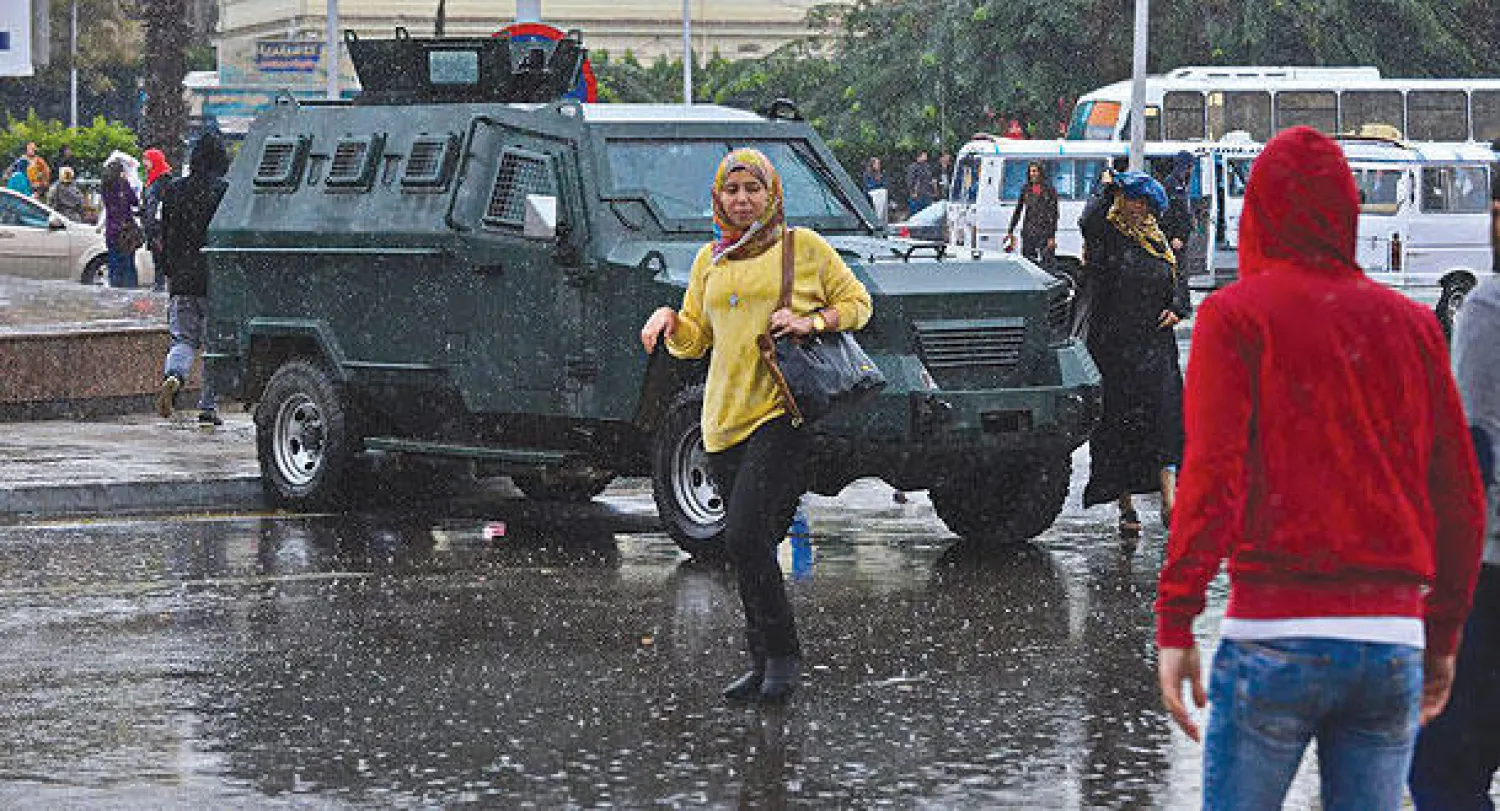 طالبة تسير بجوار عربة مصفحة تابعة للشرطة أمام جامعة القاهرة أمس وسط تساقط غزير للأمطار («الشرق الأوسط»)