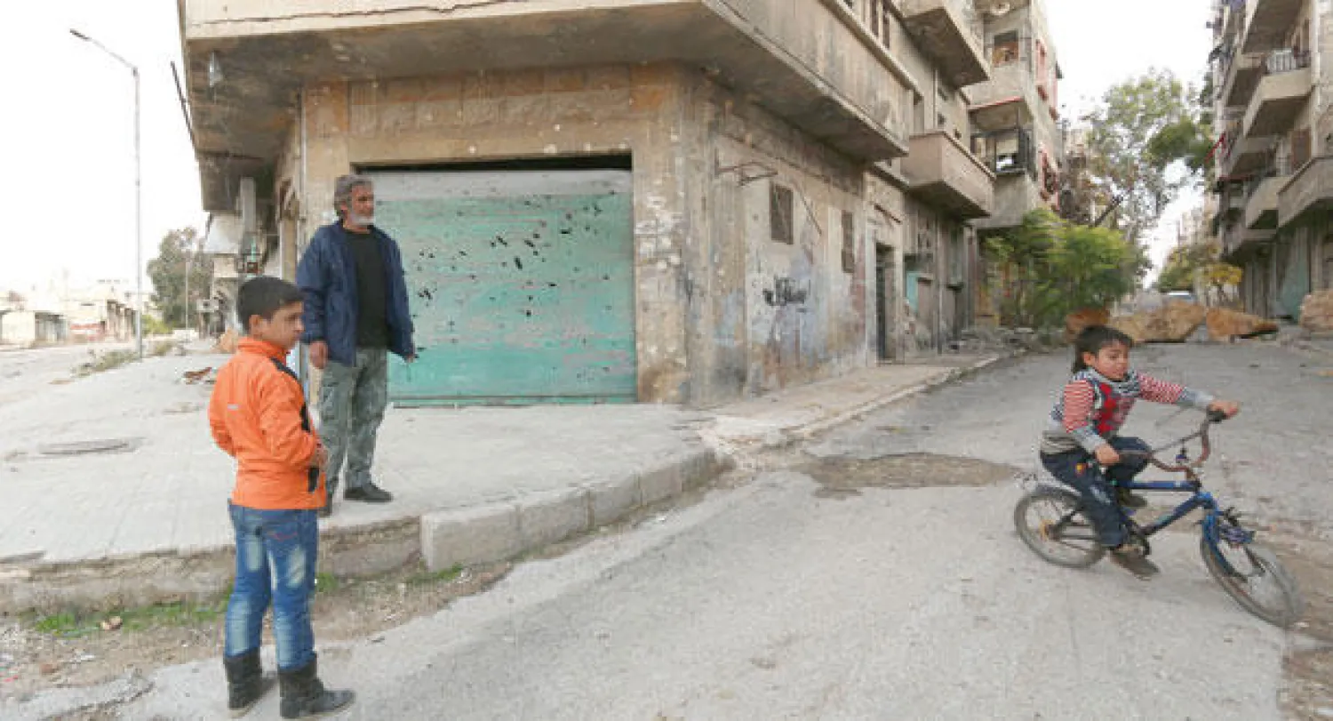 سوري يقف بجوار طفلين يلعبان في المنطقة الخاضعة للمعارضة السورية في مدينة حلب أمس (أ.ف.ب)