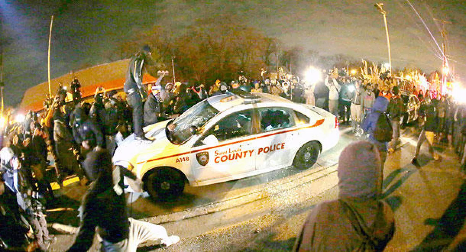 متظاهر يسكب وقودا على سيارة شرطة بهدف إضرام النار فيها بعد صدور حكم تبرئة ضابط الشرطة في فيرغسون مساء أول من أمس (أ.ب)