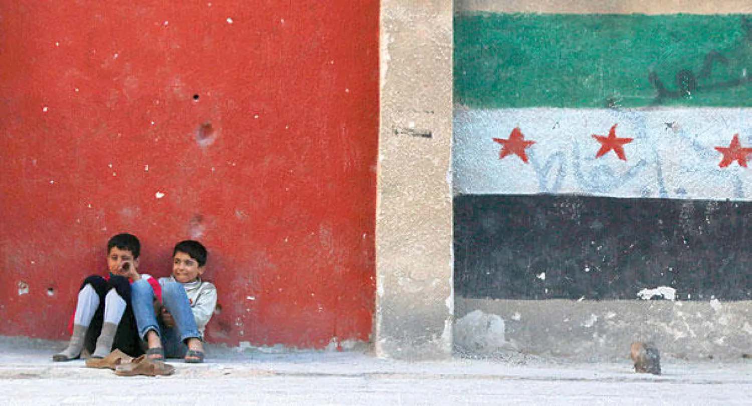 طفلان من القسم الذي تسيطر عليه المعارضة في حلب يتكآن على حائط رسم عليه علم الاستقلال الذي اتخذته المعارضة شعارا لها (رويترز)