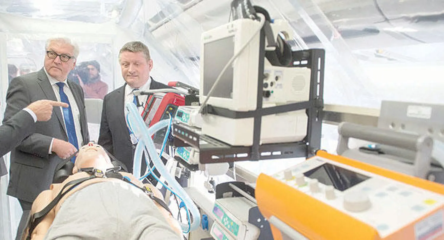 وزير الخارجية الألماني فرانك - فالتر شتاينماير (يسارا) ووزير الصحة هيرمان غروهي يقفان أمام مجسم موضوع  في «وحدة عزل صحي» داخل طائرة إيرباص جرى تخصيصها لنقل وإنقاذ المصابين بإيبولا في مطار تيغل ببرلين أمس (رويترز)