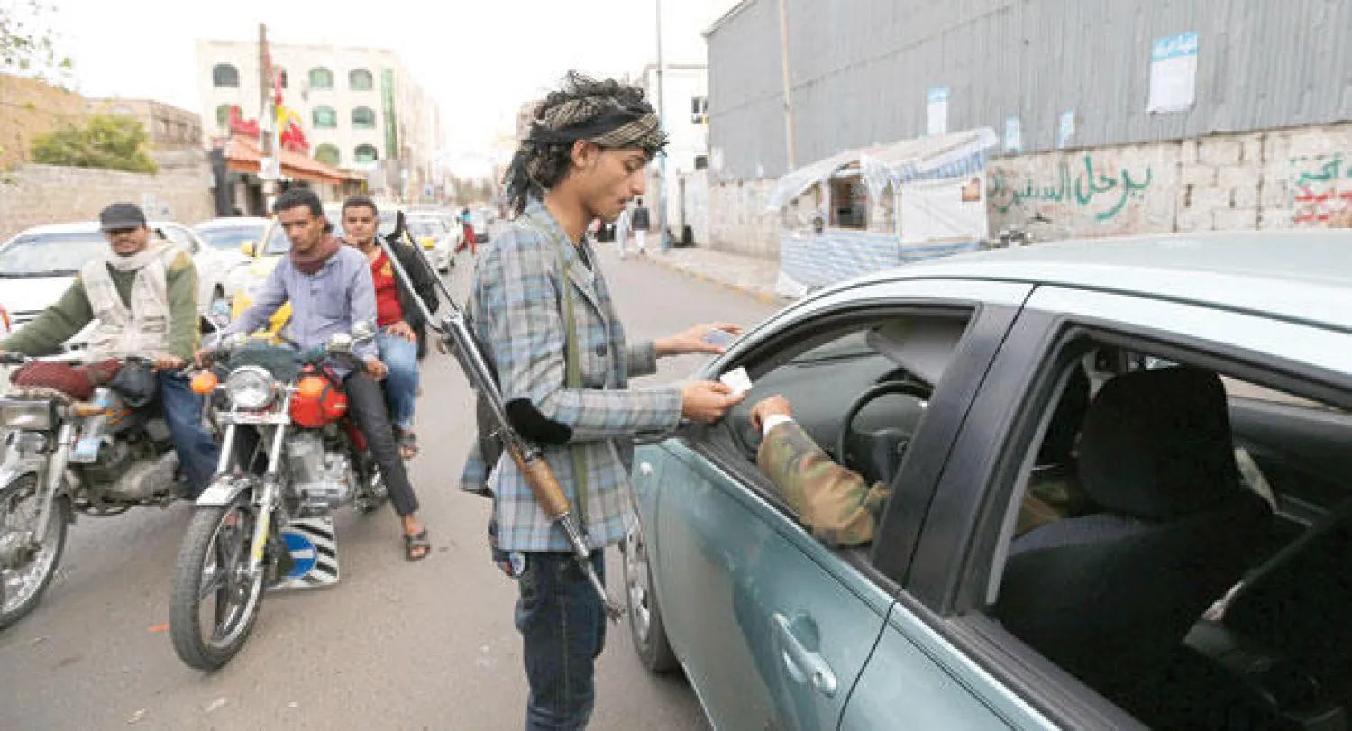 أحد عناصر الحوثيين يتفحص أوراقا ثبوتية لسائق سيارة في نقطة تفتيش بصنعاء أمس (رويترز)