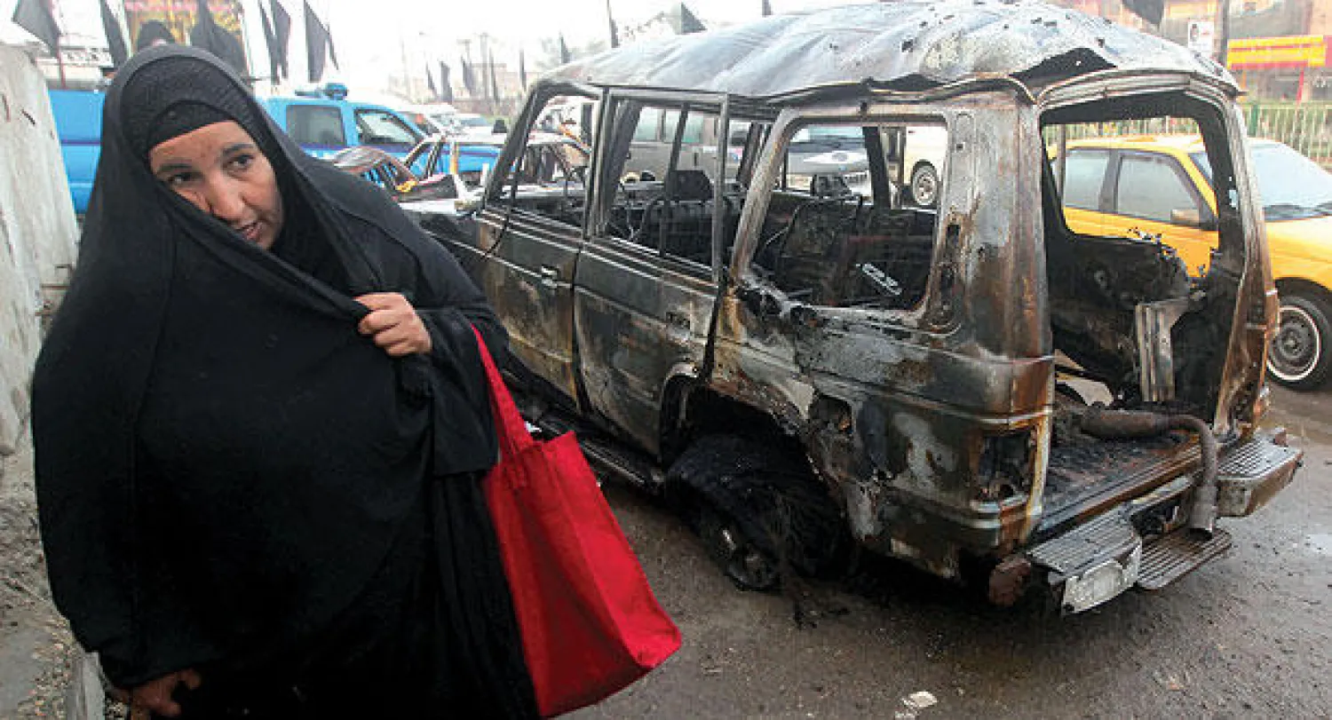عراقية تمر بالقرب من سيارة انفجرت في سوق شعبية بمدينة الصدر شرق بغداد أول من أمس (أ.ف.ب)