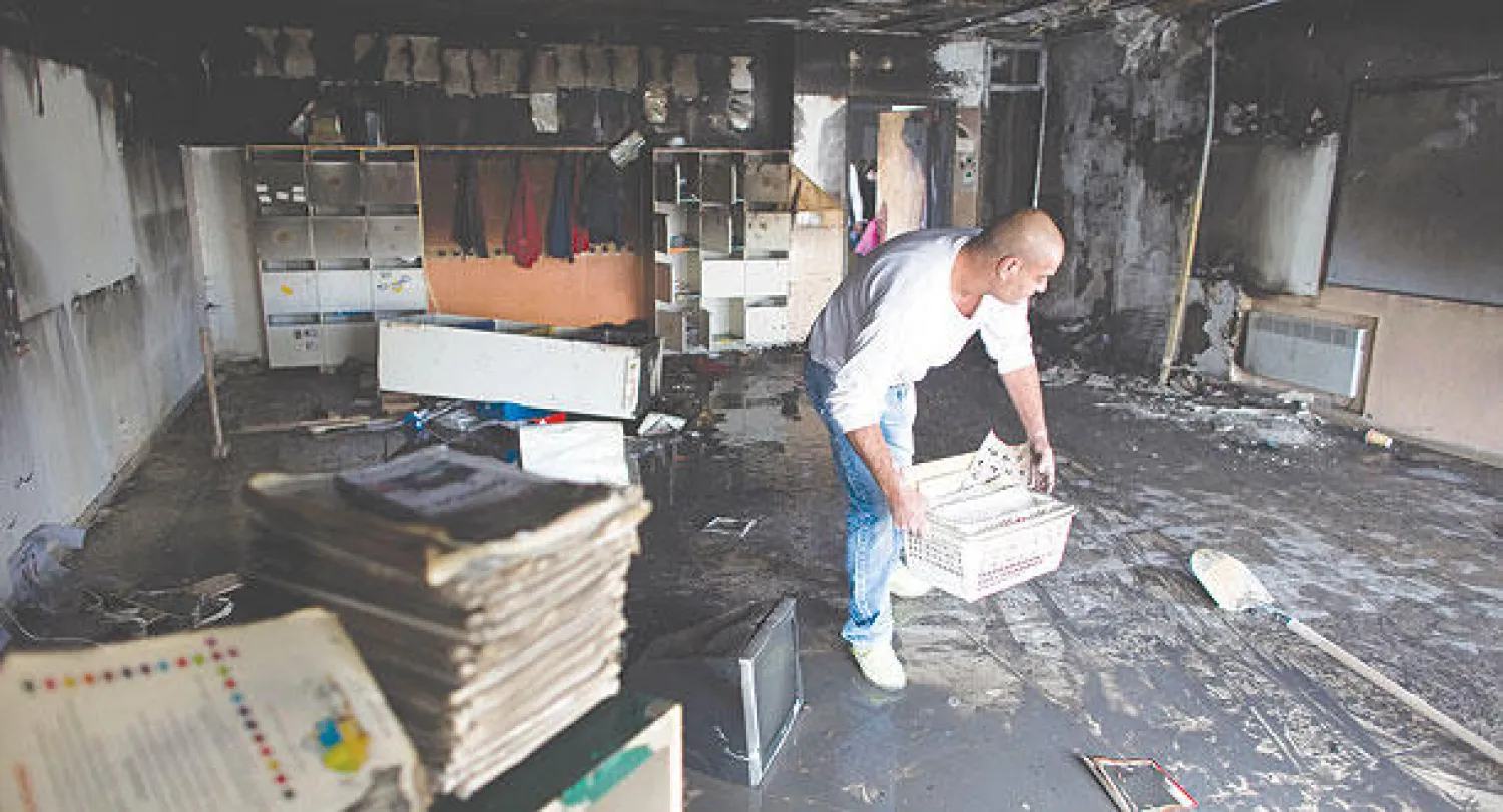 عامل يقوم بتنظيف غرفة فصل في المدرسة اليهودية - العربية بعد الحريق (رويترز)