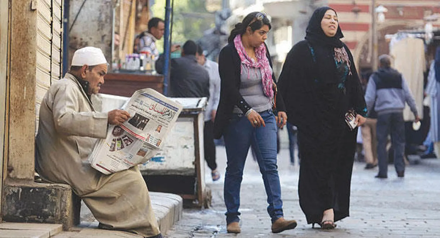 مصريتان تمران أمام رجل يتابع تداعيات الإفراج عن الرئيس المصري الأسبق حسني مبارك  عبر قراءة جريدته في شارع المعز لدين الله بالقاهرة القديمة أمس (أ.ب)