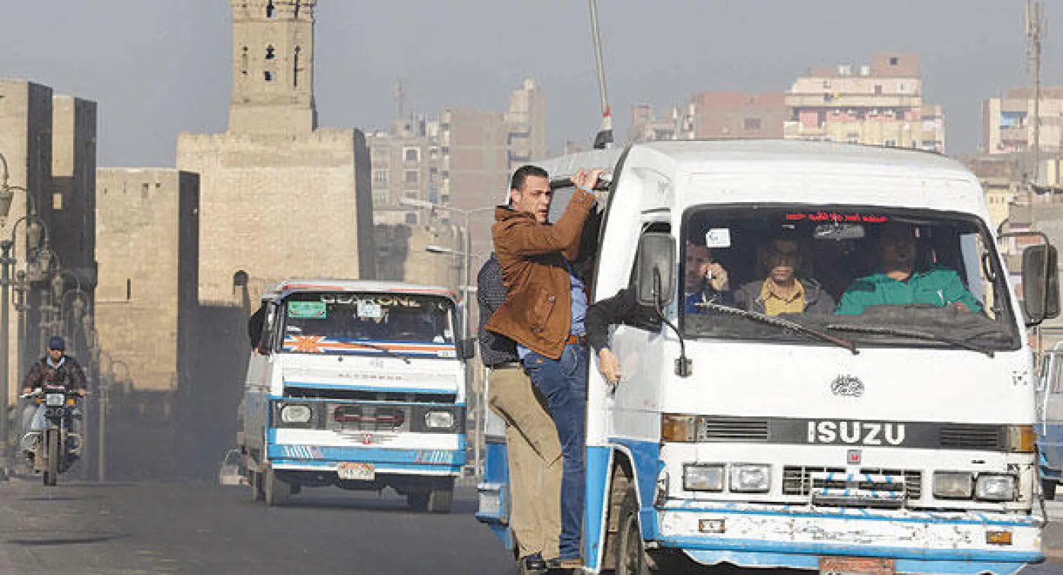 ميكروباس ازدحم بركاب مصريين في شارع بالقاهرة القديمة وتظهر في الخلف مئذنة أحد مساجد العصر الفاطمي أمس (أ.ب)