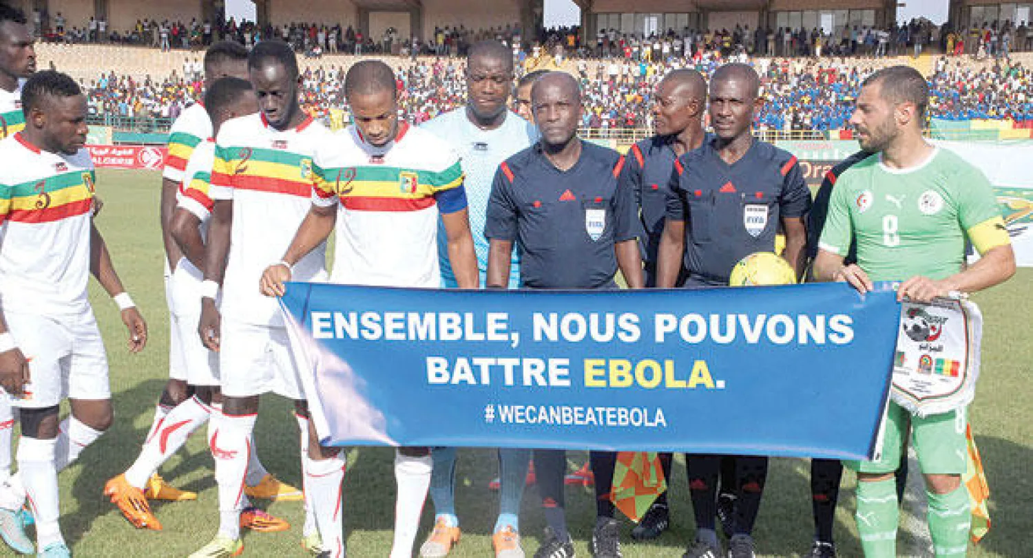 مهدي لحسن قائد المنتخب الجزائري (يمين) ولاعبو منتخب مالي يرفعون شعار {معا يمكننا مواجهة إيبولا} خلال مباراة الفريقين في تصفيات أمم أفريقيا (أ.ف.ب)