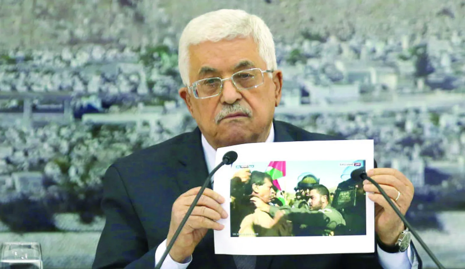 الرئيس الفلسطيني محمود عباس يحمل صورة تظهر جنودا اسرائيليين وهم يهاجمون الوزير أبو العين قبل أن يقتل على أيديهم أمس (أ.ف.ب)