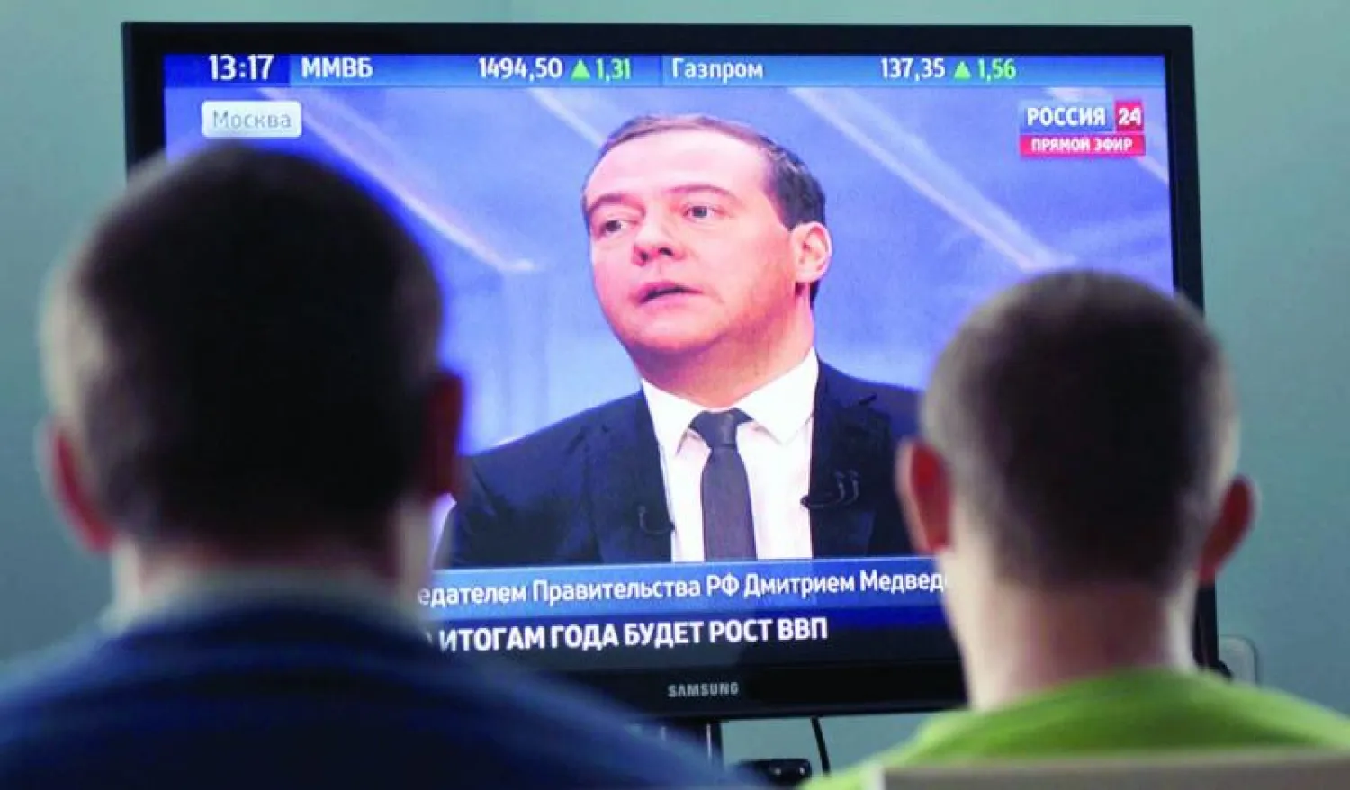 روسيان يتابعان مقابلة مع رئيس الوزراء مدفيديف وهو يتحدث عن مصاعب بلاده الاقتصادية إثر العقوبات الأخيرة (رويترز)