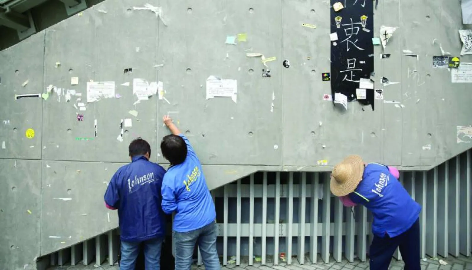 عمال يزيلون كتابات تركها المتظاهرون على جدران بحي أدميراتي في هونغ كونغ أمس (أ.ف.ب)