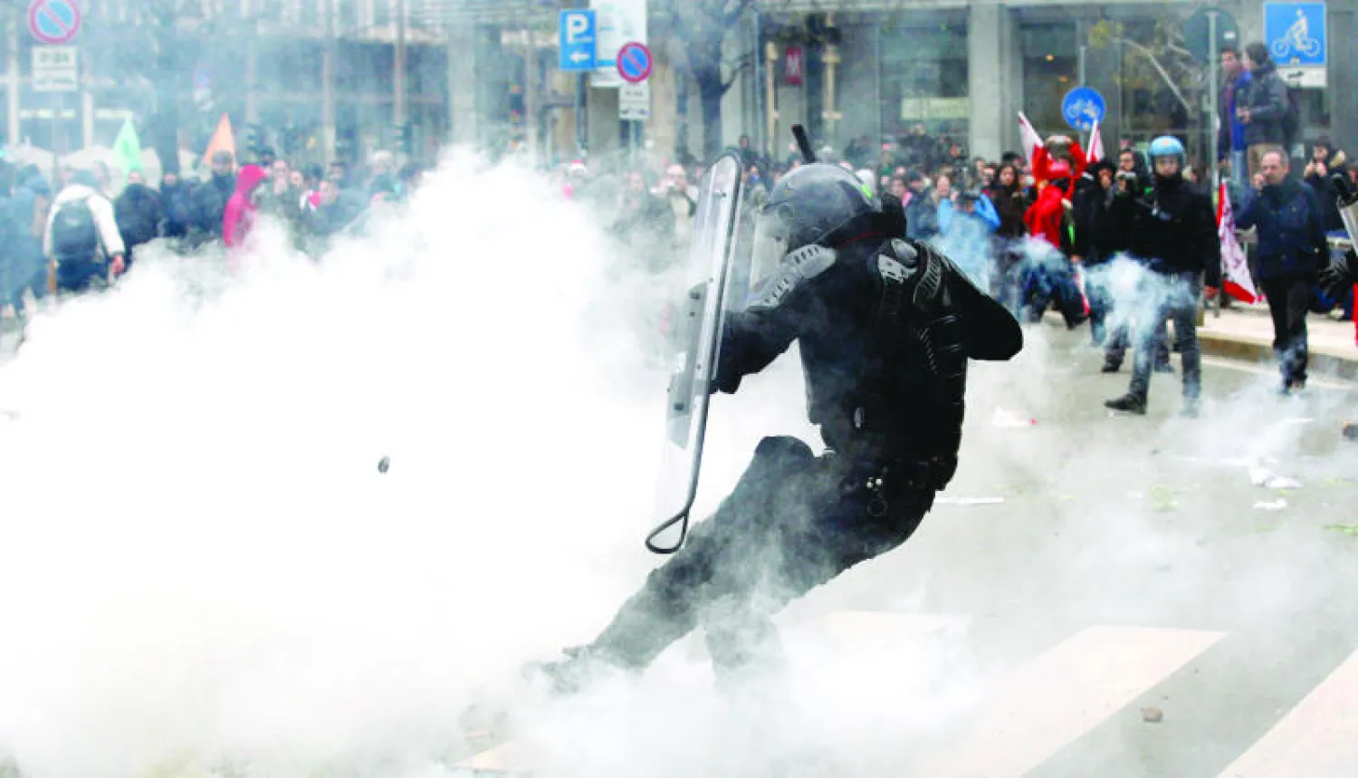 شرطي إيطالي يبعد برجله قنبلة مسيلة للدموع أثناء مواجهات مع متظاهرين محتجين على سياسات الحكومة في ميلانو أمس (أ.ب)