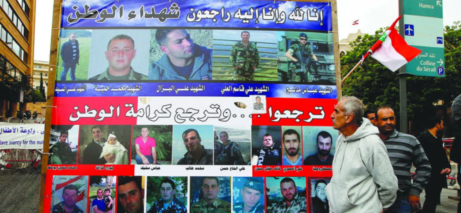 أهالي المخطوفين العسكريين بلبنان يقفون قرب ملصق كبير وسط بيروت يحمل صور من قتل أو لا يزال معتقلا لدى «النصرة» و«داعش» (إ.ب.أ)