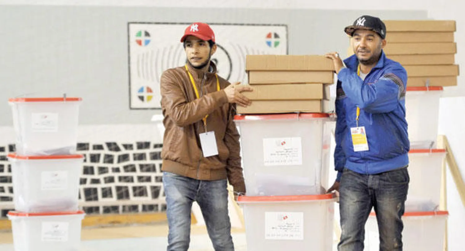 موظفان تابعان للجنة الانتخابية يحملان صناديق لتوزيعها على مراكز الاقتراع في منطقة بن عروس، أمس، استعدادا لعمليات التصويت اليوم (أ.ف.ب)