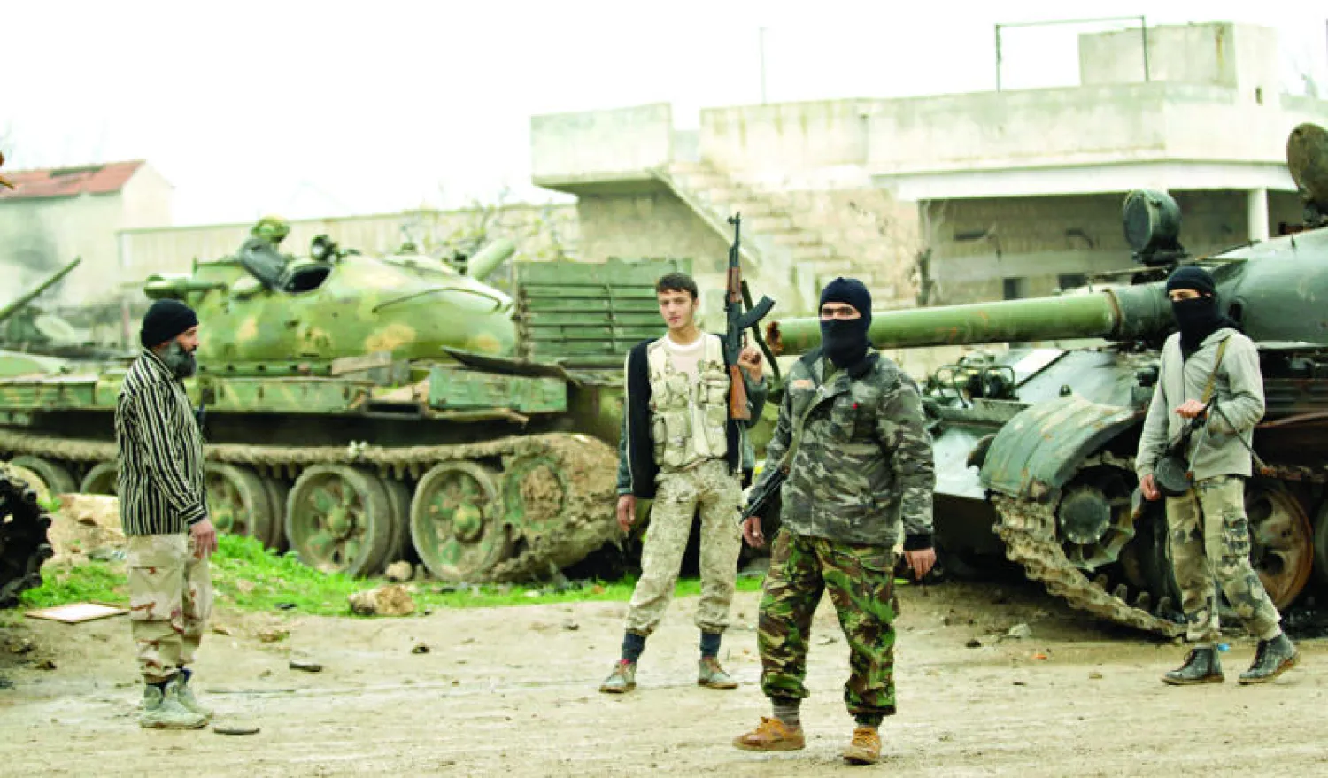 مقاتلو {أحرار الشام} يقفون إلى جانب الدبابات التي خلفتها القوات الموالية للنظام في قاعدة الحميدية في ريف إدلب الجنوبي (رويترز)