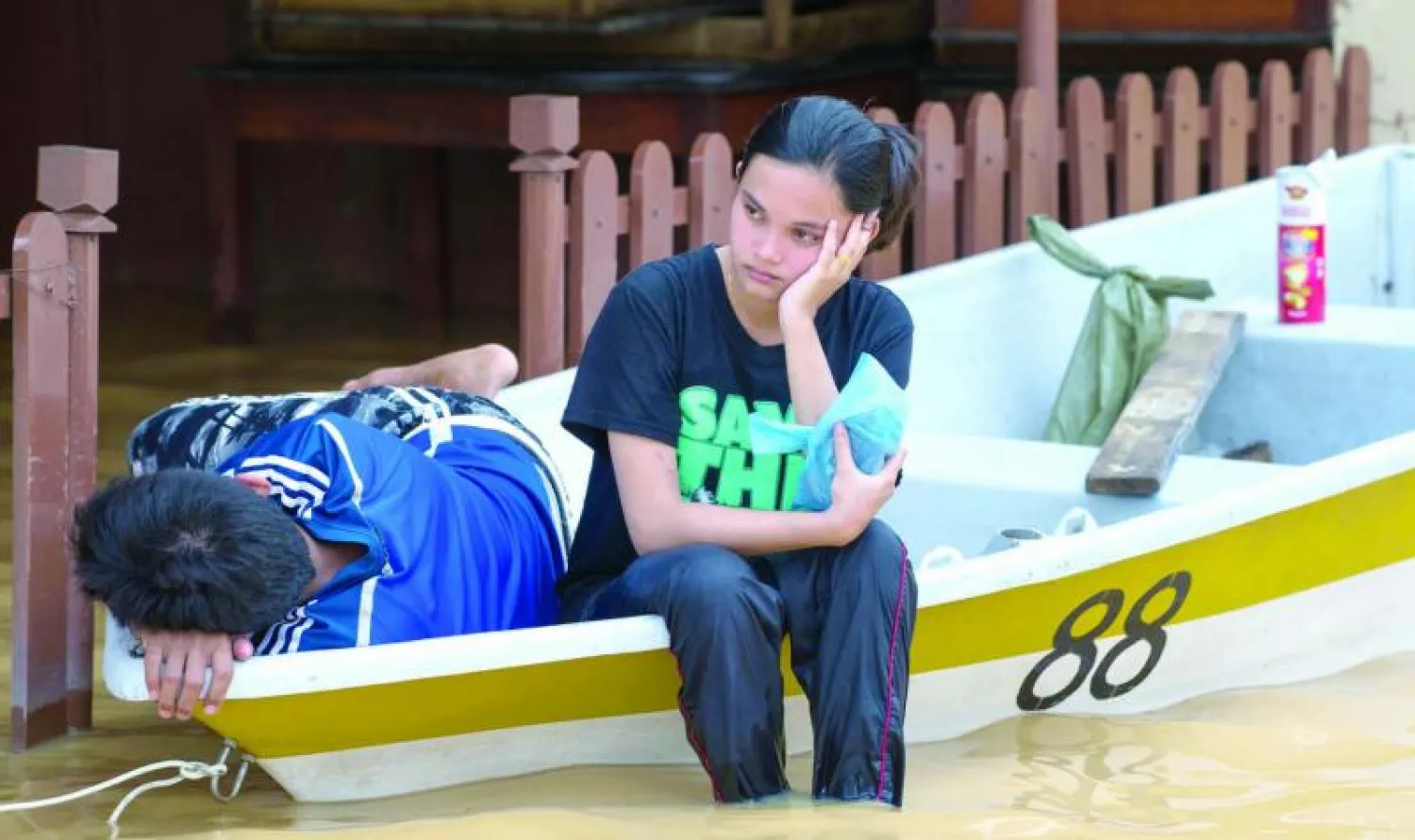 ماليزية تجلس على حافة قارب أمام منزلها الغارق في مياه الفيضانات في منطقة بينغكالان شيبا بشمال شرق ماليزيا أمس (أ.ف.ب)