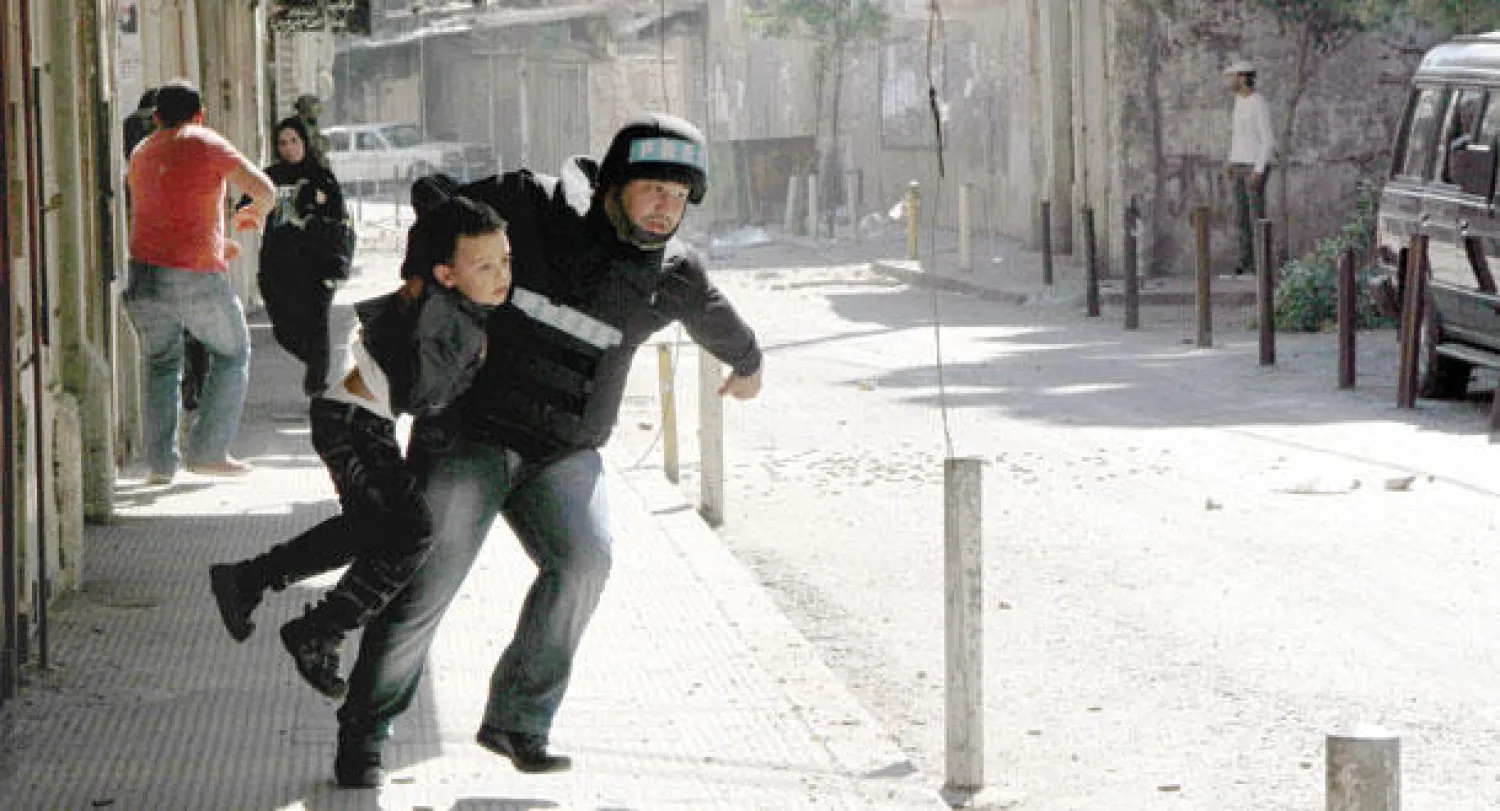 عنصر صحافي يساعد طفلا للهرب من منطقة تدور فيها اشتباكات في طرابلس في 25 اكتوبر (إ.ب.أ)