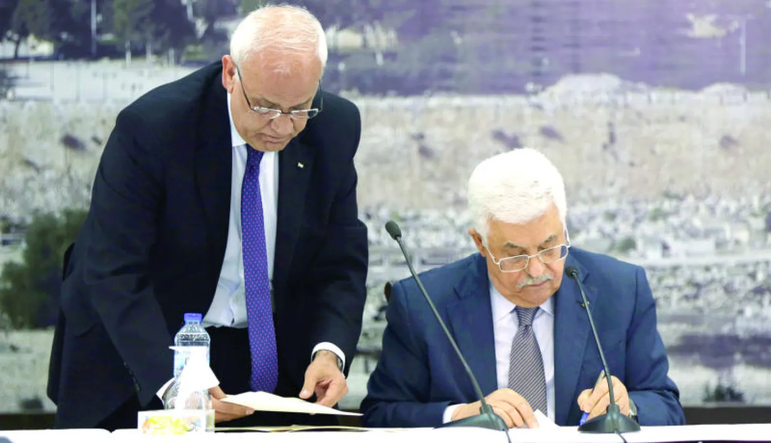 الرئيس الفلسطيني محمود عباس يوقع حزمة المعاهدات الدولية ويبدو إلى جانبه د. صائب عريقات (إ.ب.أ)