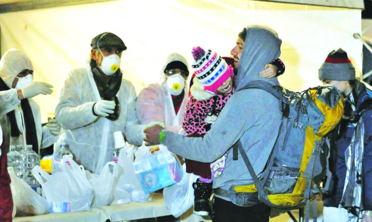 مهاجر يحمل رضيعا ويتلقى مساعدات غذائية بعد نزوله من السفينة «عز الدين» في مرفأ كوريليانو الإيطالي أمس (إ.ب.أ)