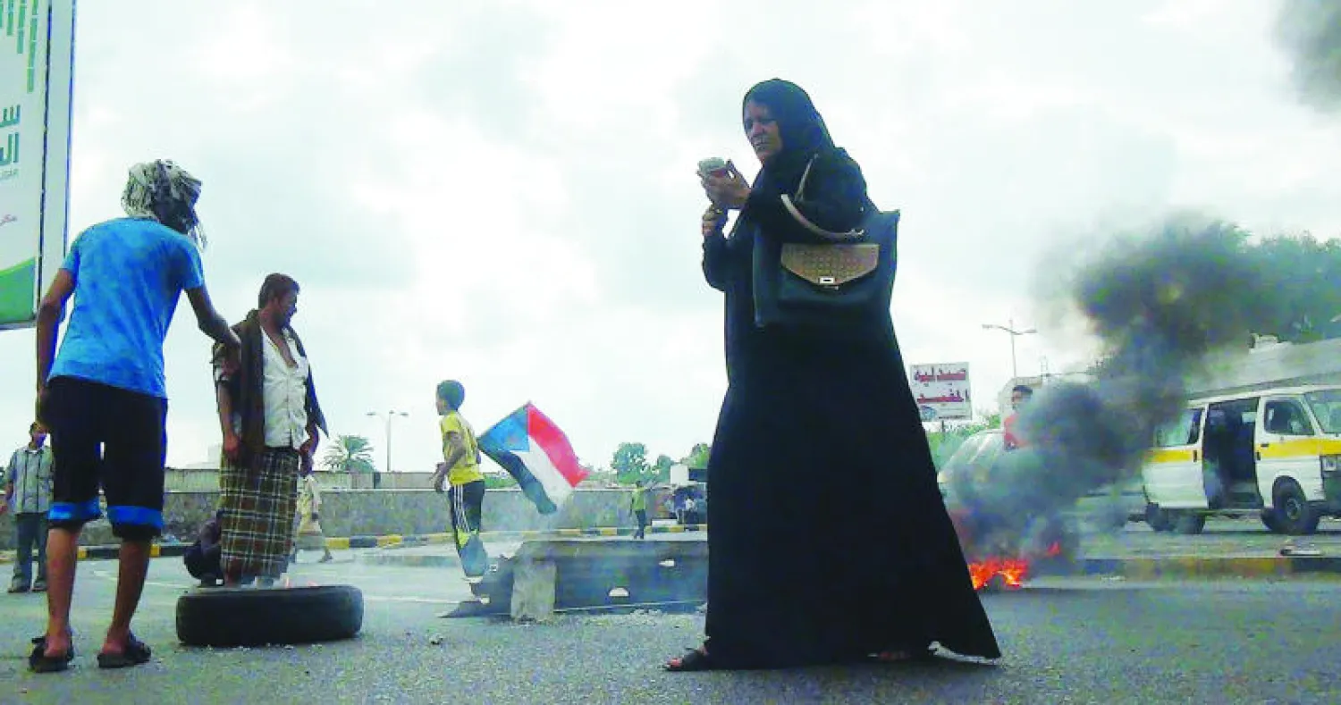 يمنية تتفحص هاتفها خلال مرورها قرب متظاهرين في عدن أمس (أ.ف.ب)