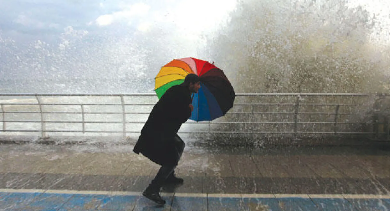 رجل يحتمي بمظلته من مياه البحر الهائج في كورنيش بيروت، أمس، مع اقتراب العاصفة «هدى ــ زينة» (رويترز)