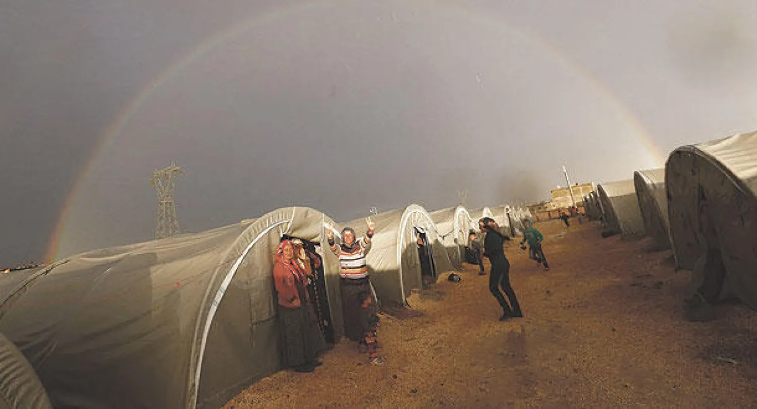 نازحون أكراد من كوباني (عين العرب) السورية يرفعون علامة النصر بينما يغطي قوس قزح مخيم سوروش التركي على الطرف الآخر من الحدود (رويترز)