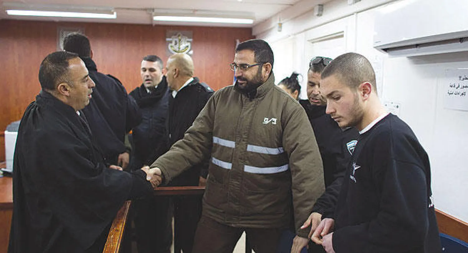 حسام القواسمة يصافح يد محاميه خلال جلسة محاكمته في محكمة أوفر بالقرب من رام الله أمس (رويترز)