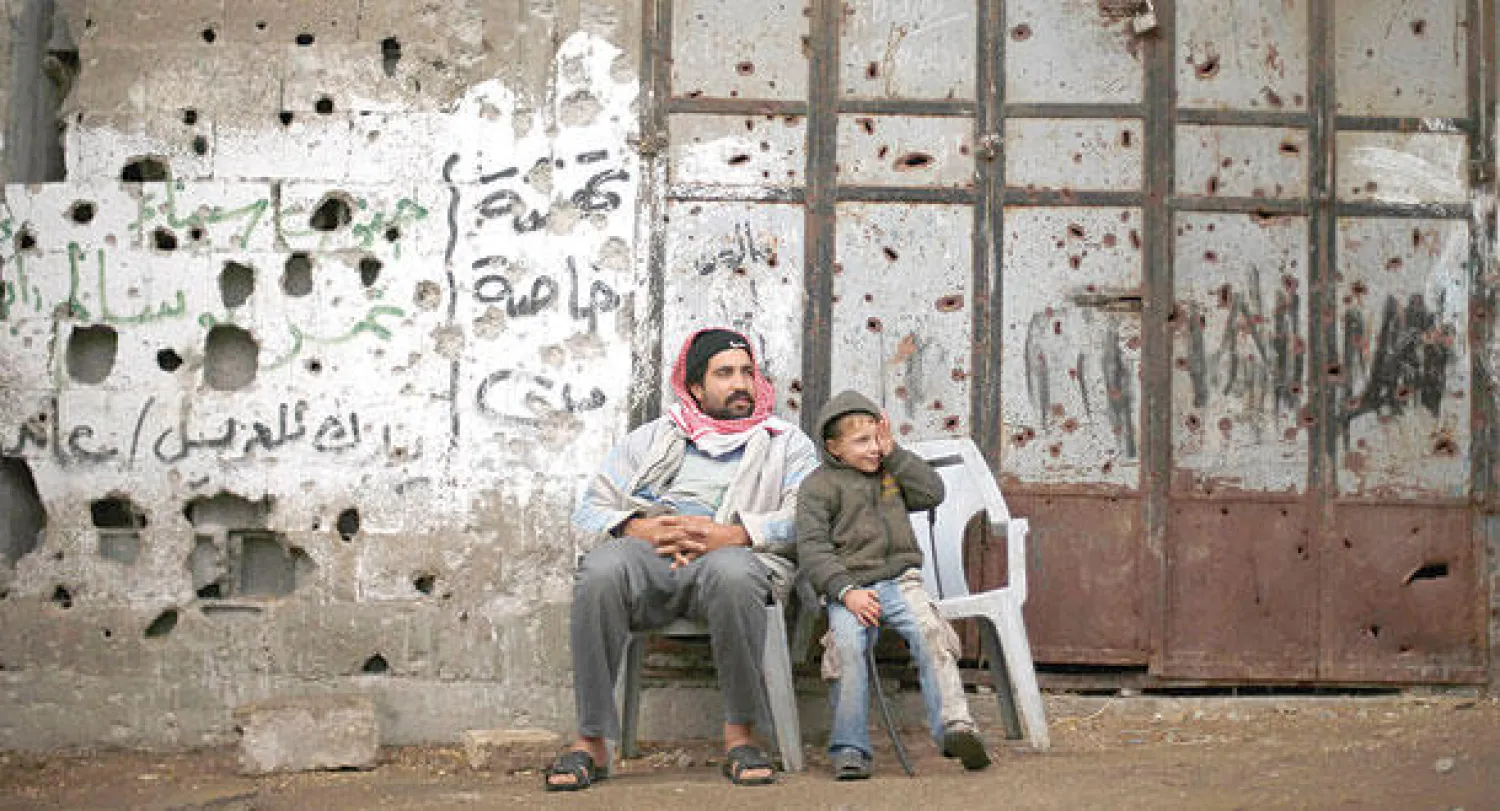 فلسطيني يجلس مع ابنه عند مدخل منزله الذي تعرض لأضرار خلال الحرب الأخيرة على غزة (رويترز)