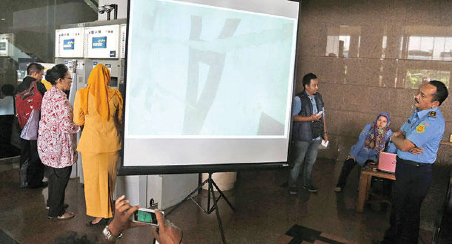 ضابط في الوكالة الإندونيسية للبحث والإنقاذ يدقق في صورة لذيل الطائرة عندما عثر عليه في أعماق البحر في جاكرتا أمس (أ.ب)