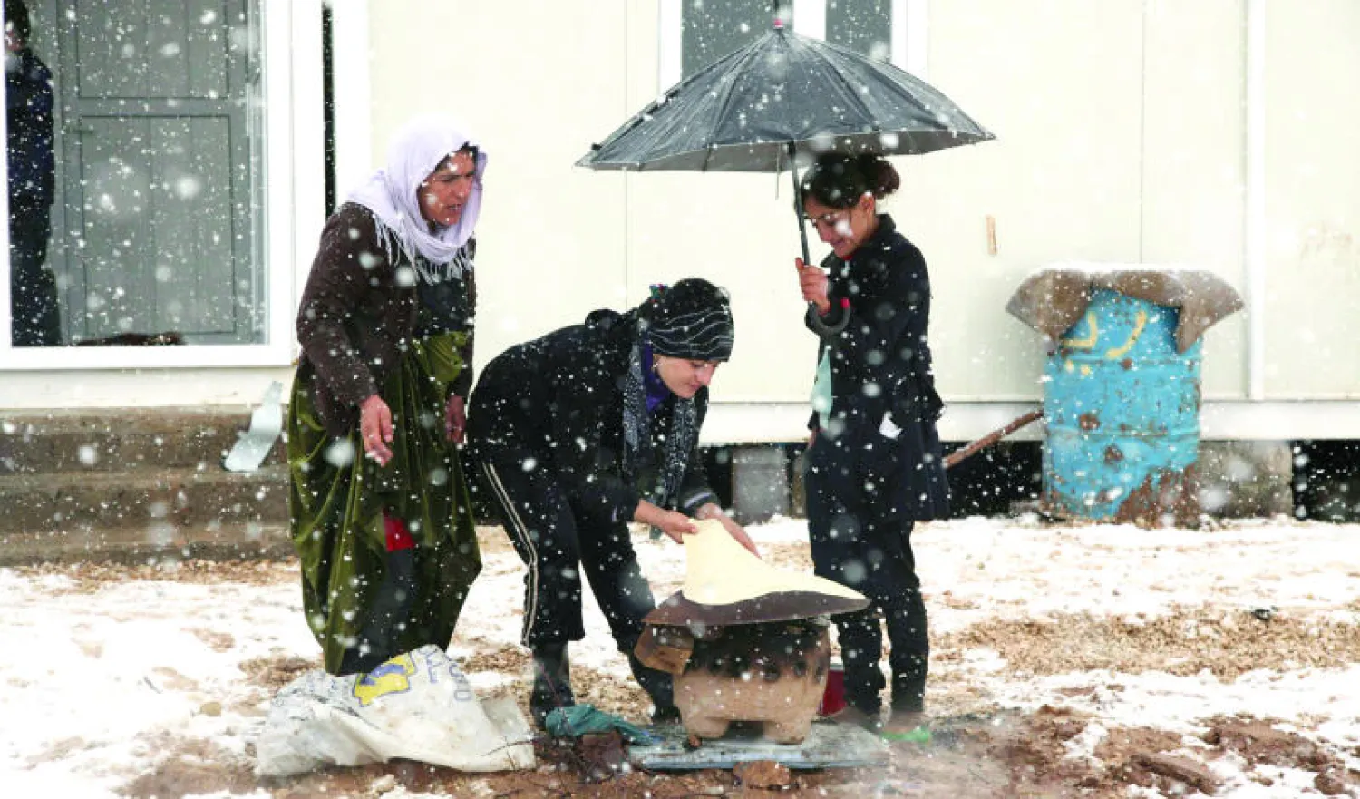إيزيديات عراقيات نازحات من سنجار في مخيم بمدينة دهوك يخبزن على «الصاج» بالطريقة المحلية وسط عاصفة ثلجية أمس (رويترز)