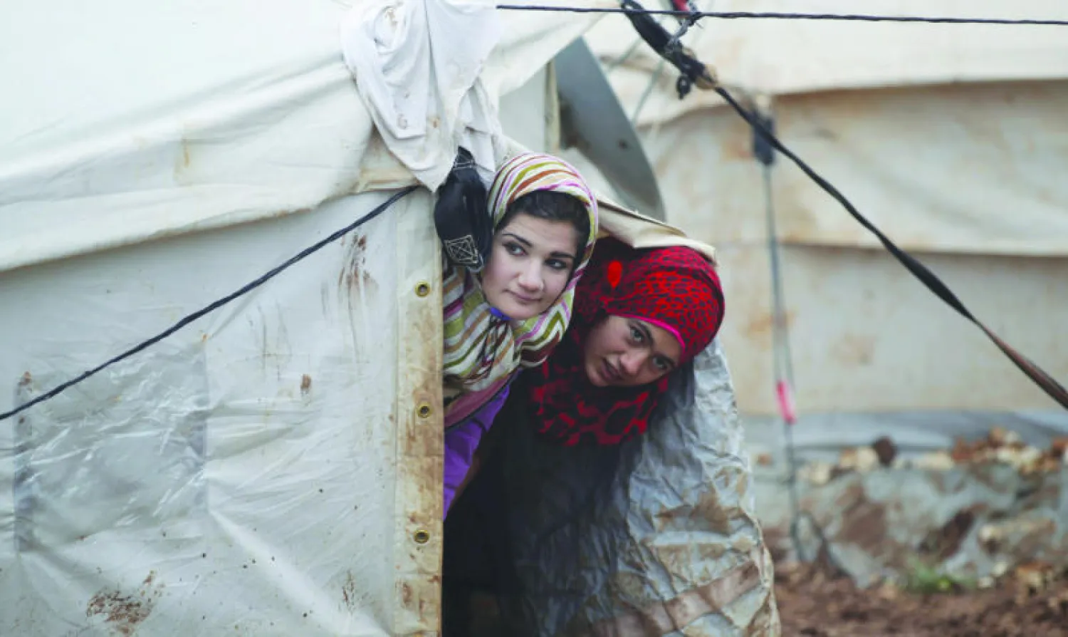 نازحتان سوريتان داخل الأراضي السورية في مخيم الكرامة قرب الحدود التركية، تتابعان من مدخل خيمتهما العاصفة الثلجية التي تسببت في أضرار جسيمة للمخيم (رويترز)
