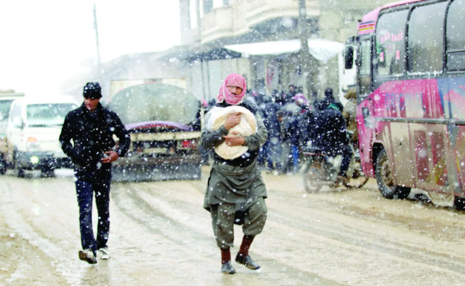 سوري يحمل ربطة خبز خلال عاصفة ثلجية في كفرنبل شمال غرب سوريا أمس (رويترز)