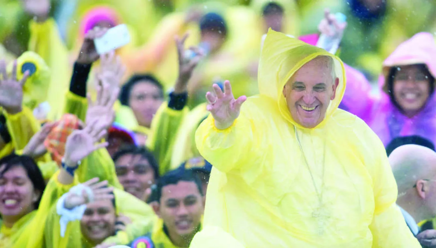 البابا يرتدي معطفا بلاستيكيا يقيه من المطر أثناء توجيهه تحية لمستقبليه في تاكلوبان بالفلبين أمس (أ.ف.ب)