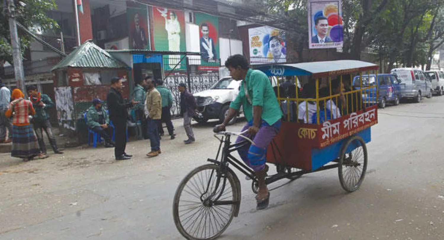 رجل ينقل تلاميذ في عربة ريكشة أمام صورة كبيرة لزعيمة المعارضة التي قررت الشرطة إنهاء وضعها قيد الإقامة الجبرية في دكا أمس (أ.ف.ب)