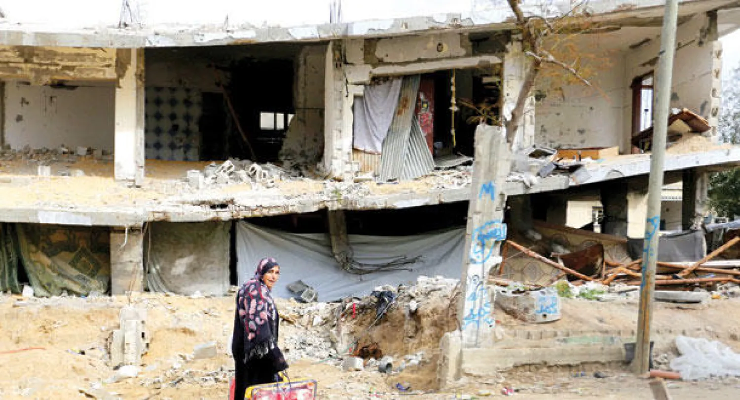 فلسطينية تسير بالقرب من مبنى دمرته إسرائيل في حرب الصيف الماضي (أ.ف.ب)