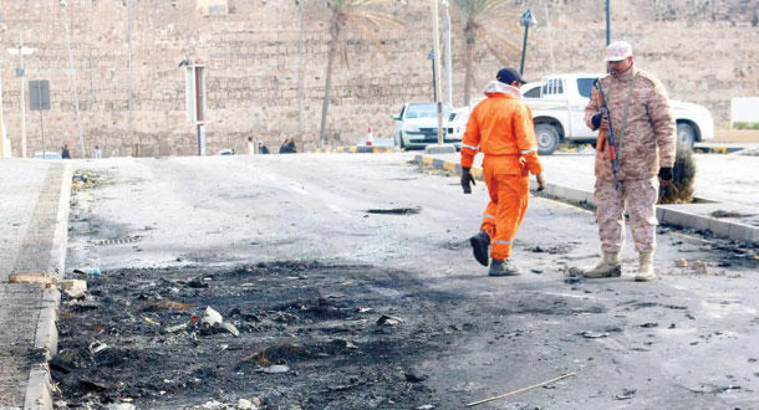 جندي ليبي مع عامل نظافة في مكان التفجير الذي استهدف فندق كورينثيا في العاصمة طرابلس (إ.ب.أ)